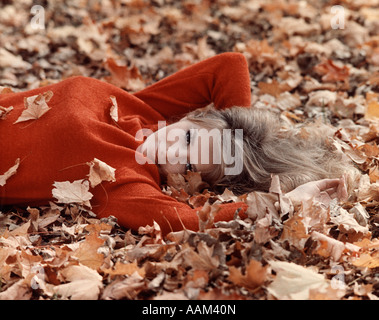 1970s PORTRAIT BLOND WOMAN SMILING LAYING  AUTUMN TREE LEAVES Stock Photo