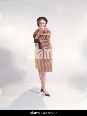 1960s WOMAN IN YELLOW DRESS BLACK HAT GLOVES SHOES PEARL NECKLACE FUR COAT Stock Photo