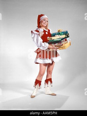1960s YOUNG WOMAN IN CHRISTMAS SANTA HELPER RED AND WHITE COSTUME AND CAP HOLDING PILE OF GIFT WRAPPED PRESENTS Stock Photo