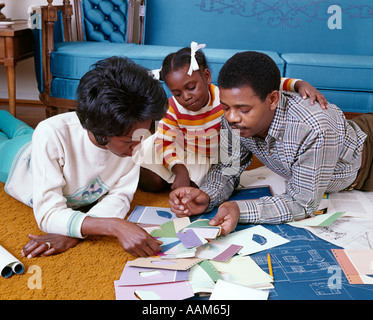 1960s AFRICAN-AMERICAN FAMILY OF 3 LOOK AT PAINT CHIPS BLUEPRINTS COLOR SAMPLES NEW HOME REDECORATE MOM DAD GIRL Stock Photo