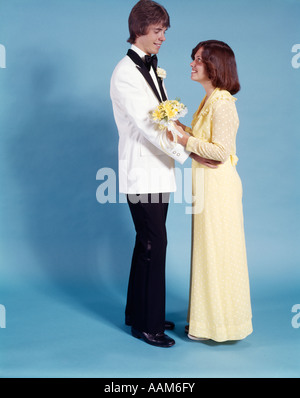 TEEN COUPLE BOY GIRL STANDING FACING ONE ANOTHER DATE TEENAGE FORMAL PROM DRESS 1970 1970s DANCE DATES PROMS TUXEDO GOWN Stock Photo