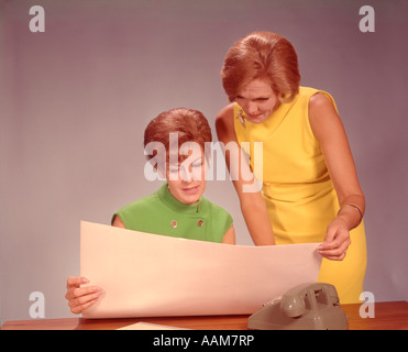 1960s TWO WOMEN EXECUTIVES AT DESK WITH TELEPHONE LOOKING AT WORKSHEET Stock Photo