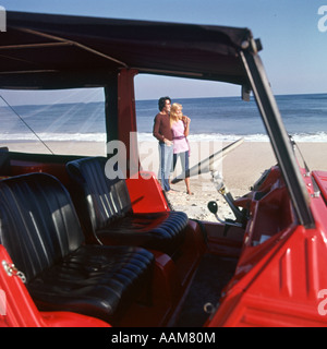 COUPLE ON BEACH STANDING OUTSIDE VEHICLE Stock Photo