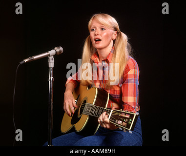1970 1970s BLOND BLONDE YOUNG WOMAN PIGTAILS PLAID SHIRT JEANS PLAY GUITAR SINGING MICROPHONE FOLK SINGER SINGERS Stock Photo