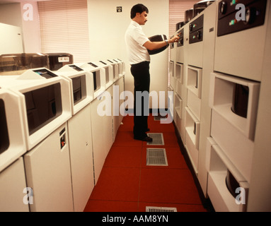 1970s 1980s COMPUTER TECHNICIAN CHANGE REEL ON MAIN FRAM COMPUTER RED & WHITE ROOM Stock Photo