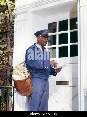 1960s AFRICAN-AMERICAN MAN MAILMAN RETRO CARRYING MAILBAG SORTING LETTERS FRONT DOOR DELIVERY DELIVERING USPS Stock Photo