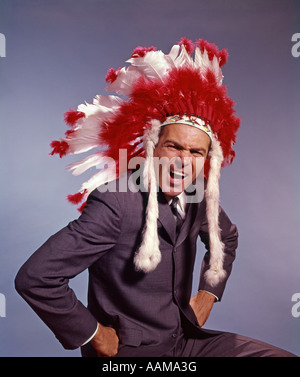 1970s MAN IN NATIVE AMERICAN COSTUME HEADDRESS AND SUIT WITH HANDS ON HIPS SYMBOLIC EXPRESSION EXECUTIVE Stock Photo