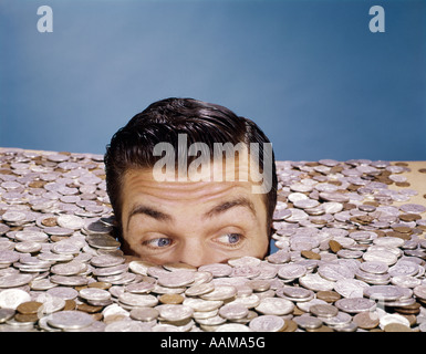 TOP OF HEAD AND EYES OF MAN LOOKING OUT FROM PILE OF COINS STUDIO SYMBOLIC CURRENCY Stock Photo