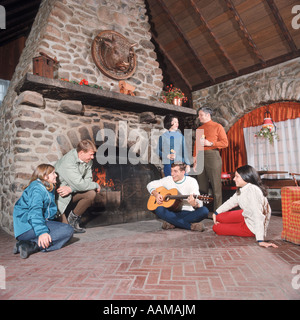 ADULTS INSIDE SKI LODGE SITTING AROUND THE FIRE PLAYING GUITAR Stock Photo