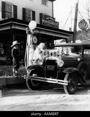 ELDERLY GRANDFATHER FILLING UP FORD CAR IN FRONT OF PENNSYLVANIA GENERAL STORE WITH GRANDSON WATCHING 1930s Stock Photo