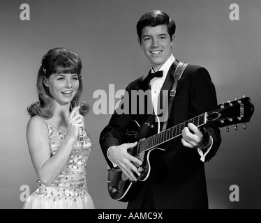 1960s TEENAGE ENTERTAINMENT DUO MAN PLAYING GUITAR AND WOMAN SINGING HOLDING MICROPHONE Stock Photo