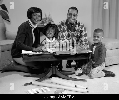 1960s SMILING AFRO-AMERICAN FAMILY SEATED BEHIND COFFEE TABLE LOOKING AT BLUEPRINTS Stock Photo