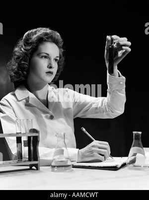 1940s STUDENT NURSE HOLDING UP TEST TUBE WHILE TAKING NOTES IN SCIENCE CLASS Stock Photo