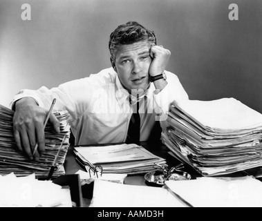 1950s PORTRAIT MAN OVERWORKED WITH DESK FULL OF PAPERS Stock Photo