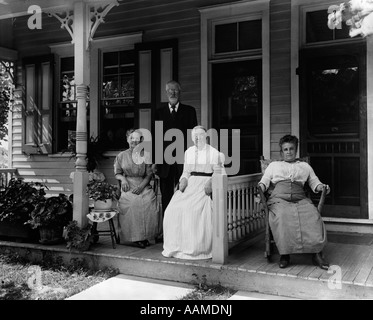 1890s 1900s TURN OF THE CENTURY GROUP OF FOUR NEIGHBORS SITTING ON THE PORCH OF A DUPLEX Stock Photo