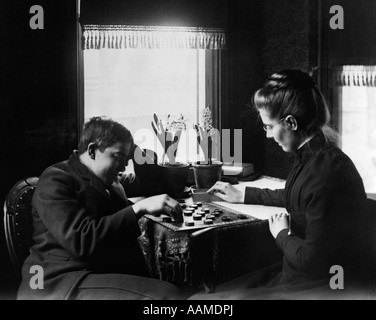 1890s 1900s TURN OF THE CENTURY YOUNG MAN BROTHER AND YOUNG WOMAN SISTER PLAYING CHECKERS Stock Photo