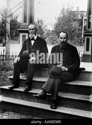 1890s TURN OF THE CENTURY TWO BEARDED MEN FATHER AND SON IN SUITS HOLDING BOWLER HATS SITTING ON STAIRS IN FRONT OF HOUSE Stock Photo