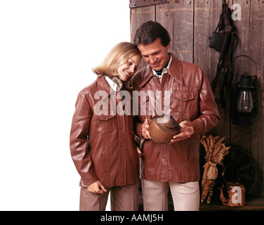 1970 1970s COUPLE MAN WOMAN WEARING MATCHING LEATHER JACKETS LOOKING AT ANTIQUE POT FASHION CLOTHES RETRO Stock Photo