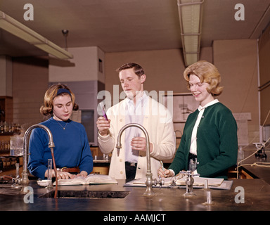 1960 1960s 3 STUDENTS IN CHEMISTRY LAB CLASS LABORATORY EXPERIMENT SCIENCE HIGH SCHOOL BOY GIRLS TEENS RETRO Stock Photo