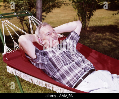 1960s OLDER MAN LYING IN HAMMOCK IN YARD RETIRED LIFESTYLE LEISURE Stock Photo