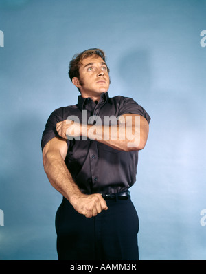 1970s MUSCULAR YOUNG MAN ROLLING UP SHIRT SLEEVE SYMBOLIC READY TO WORK INTENT DETERMINED Stock Photo