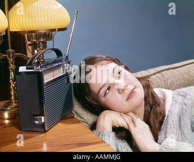 1960s TEEN GIRL LYING ON COUCH LISTENING TO TRANSISTOR RADIO MUSIC RETRO VINTAGE Stock Photo