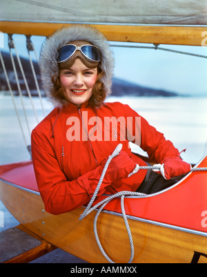 1960s WOMAN SITTING IN COCKPIT OF ICE BOAT HOLDING ROPES FOR SAIL GLOVES FUR HAT GOGGLES Stock Photo