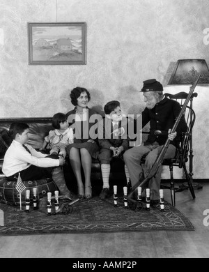 1920s 1930s MOTHER AND THREE CHILDREN LISTENING TO GRANDFATHER IN CIVIL WAR UNION UNIFORM HOLDING RIFLE TELL STORIES Stock Photo