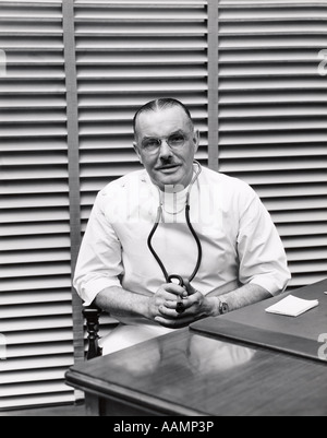 1940s PORTRAIT OF DOCTOR SITTING BEHIND DESK SMILING Stock Photo