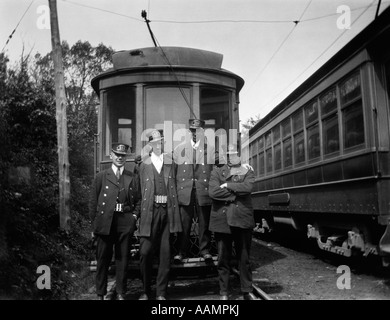 1910s 1920s 4 MEN CONDUCTORS MOTORMEN PUBLIC TRANSPORTATION TRANSIT WORKERS POSING IN FRONT OF TROLLEY CAR IN UNIFORMS AND HATS Stock Photo
