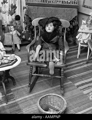 VICTORIAN DOLL SITTING CROSS-LEGGED ON SMALL ROCKING CHAIR Stock Photo