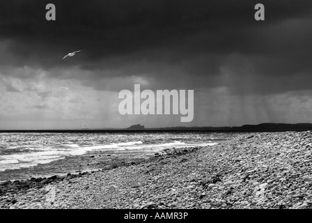 Black and white image of storm clouds over Bamburgh Castle seen from the Holy Island of Lindisfarne Northumberland Stock Photo
