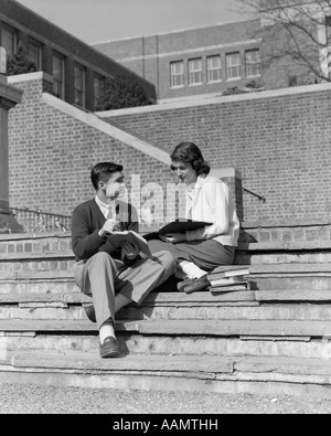 1950s TEENAGE MAN WOMAN SITTING ON STEPS OUTSIDE OF SCHOOL COLLEGE BOOKS NOTES ON LAP STUDYING TALKING Stock Photo