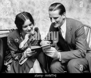 1920s 1930s COUPLE READING SHARING BOOK SMILING MAN POINTING OUT PASSAGE TO WOMAN