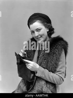 1930s 1940s WOMAN DRESSED UP WITH FUR JACKET HOLDING PURSE AND MONEY LOOKING AT CAMERA Stock Photo