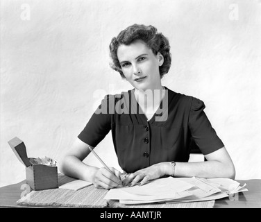 1940s WOMAN AT DESK GOING THROUGH PAPERWORK PAYING BILLS LOOKING AT CAMERA Stock Photo
