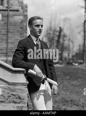 1930s YOUNG MAN LEANING ON STONE WALL STUDENT GRADUATE HOLDING DIPLOMA Stock Photo