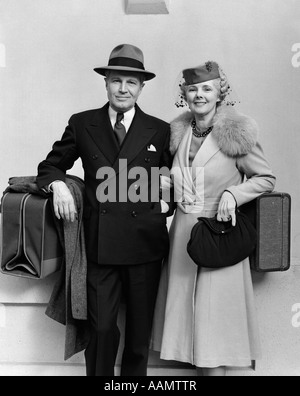 1930s 1940s OLDER COUPLE DRESSED UP WITH LUGGAGE LOOKING AT CAMERA Stock Photo