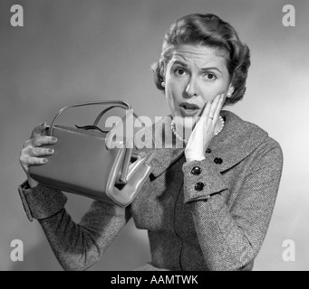 1950s BROKE WOMAN SURPRISED FACIAL EXPRESSION HAND TO CHEEK HOLDING EMPTY HANDBAG LOOKING AT CAMERA Stock Photo