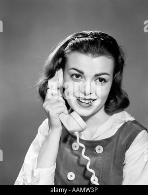 1950s TEENAGE GIRL TALKING ON WALL MOUNTED DIAL TELEPHONE HOLDING THE ...