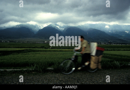 Chinese Man cycling through countryside as storm brews, Dali, Yunnan province, China Stock Photo