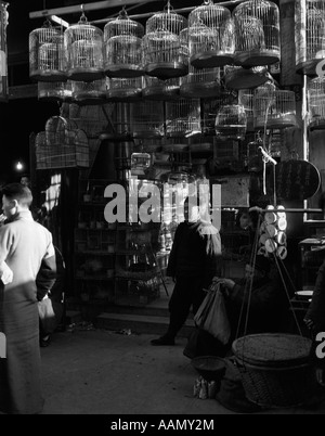 1920s 1930s CHINESE MAN MERCHANT STANDING IN FRONT OF BIRD MARKET HANGING BIRDCAGES SHOP SHANGHAI CHINA Stock Photo