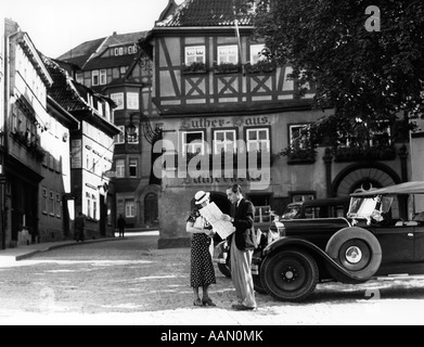 1930s TOURIST COUPLE BY CAR LOOKING AT MAP IN FRONT OF EISENACH LUTHERHAUS 1563 WHERE LUTHER LIVED WHILE ATTENDING SCHOOL Stock Photo