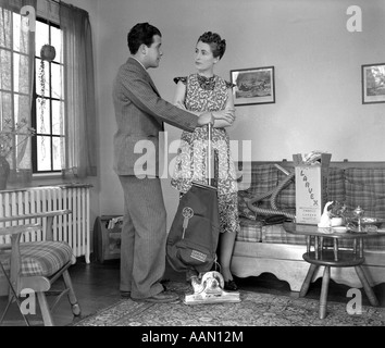 1930s 1940s SALESMAN IN SUIT DEMONSTRATING VACUUM CLEANER BY A WINDOW IN A LIVING ROOM TO A LADY WEARING A PRINT DRESS Stock Photo