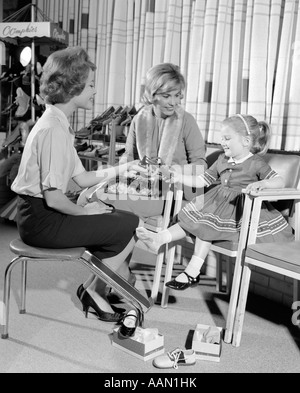 1960s MOTHER DAUGHTER SHOE SHOPPING SALESWOMAN SHOWING PATENT LEATHER SHOE TO GIRL IN RETAIL STORE Stock Photo