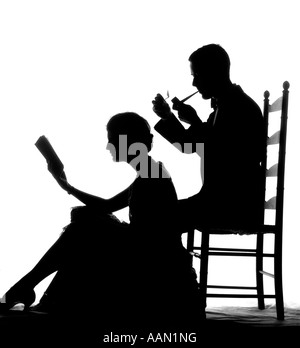 1920s 1930s ANONYMOUS SILHOUETTED MAN IN LADDER-BACK CHAIR SMOKING PIPE WITH WOMAN SEATED ON FLOOR IN FRONT OF HIM READING BOOK Stock Photo