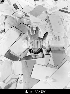 1950s MAN HAND STICKING OUT OF PILE OF MAIL BILLS LETTERS DROWNING Stock Photo