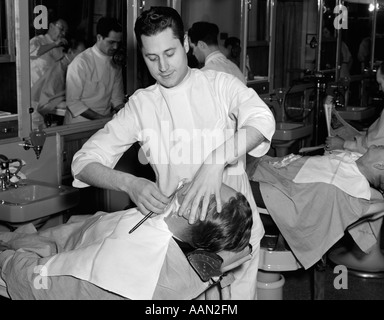 1940s MAN LEANING BACK IN CHAIR GETTING A SHAVE WITH A STRAIGHT RAZOR FROM BARBER IN WHITE TUNIC Stock Photo