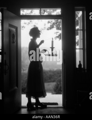 1920s SILHOUETTE OF WOMAN STANDING IN DOORWAY CARRYING CANDLE HOLDER Stock Photo