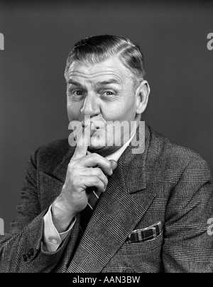 1940s ELDERLY MAN WEARING SUIT MAKING SHUSH GESTURE LOOKING AT CAMERA Stock Photo